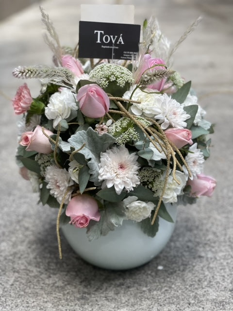 Arreglo de rosas con claveles y follaje, sobre florero de cerámica.