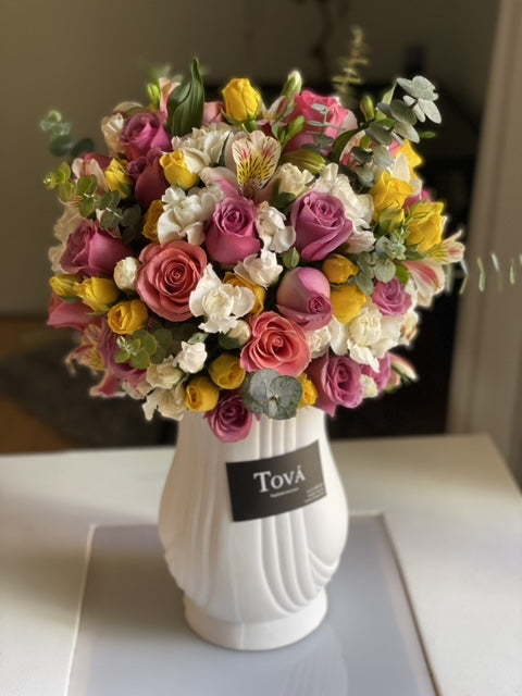 Arreglo floral con rosas de invernadero, mini rosas, claveles y follaje sobre florero.