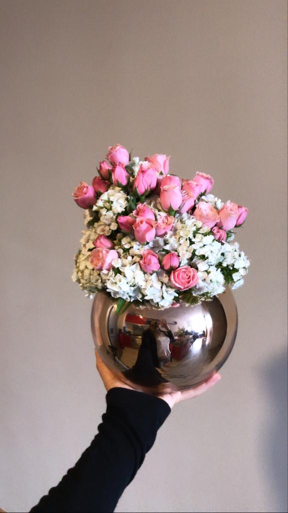 Mini rosa con follaje sobre florero de vidrio.