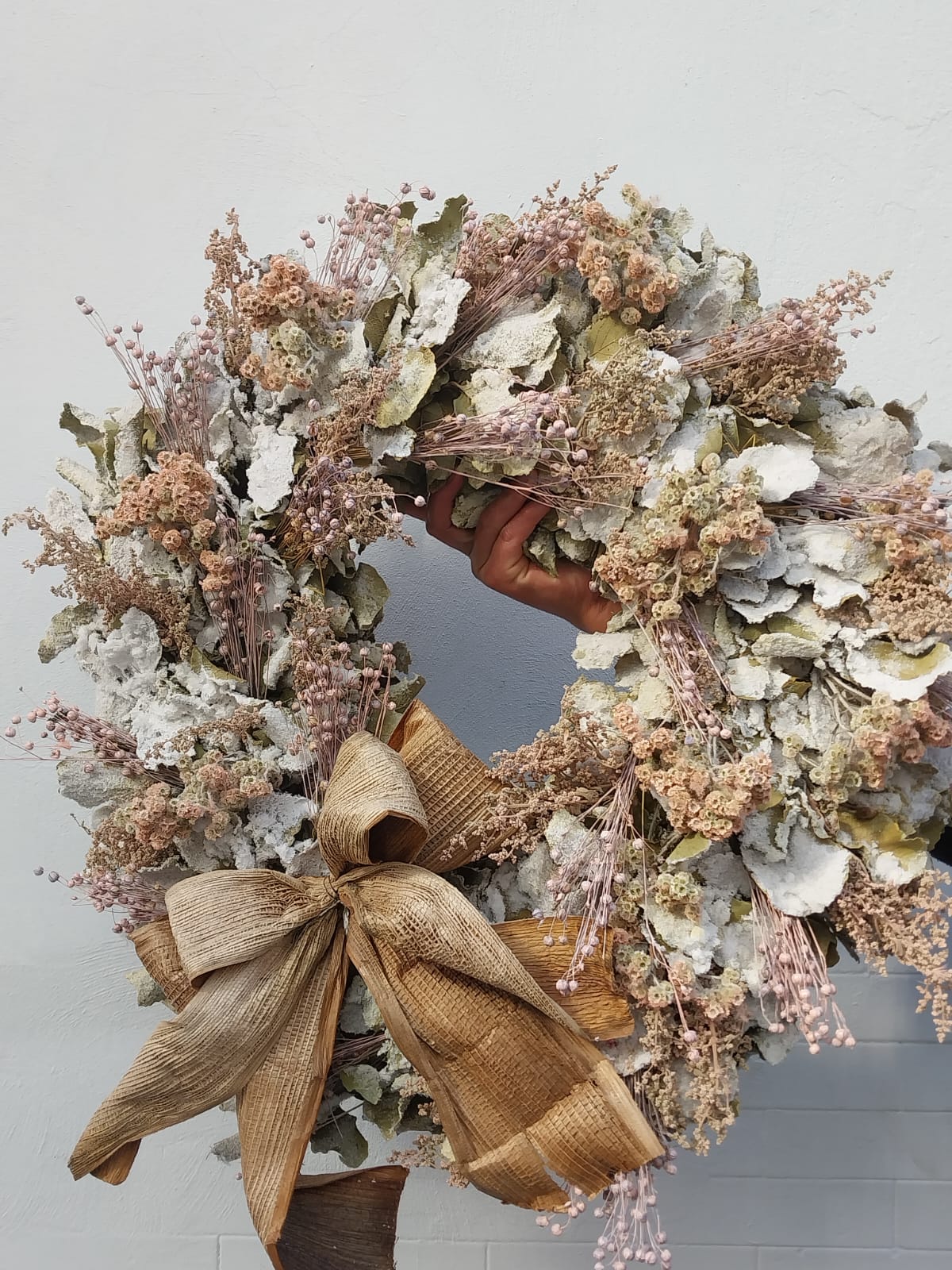 Corona navideña para pared o puerta hecha a mano con un conjunto de flores y follaje preservado.
