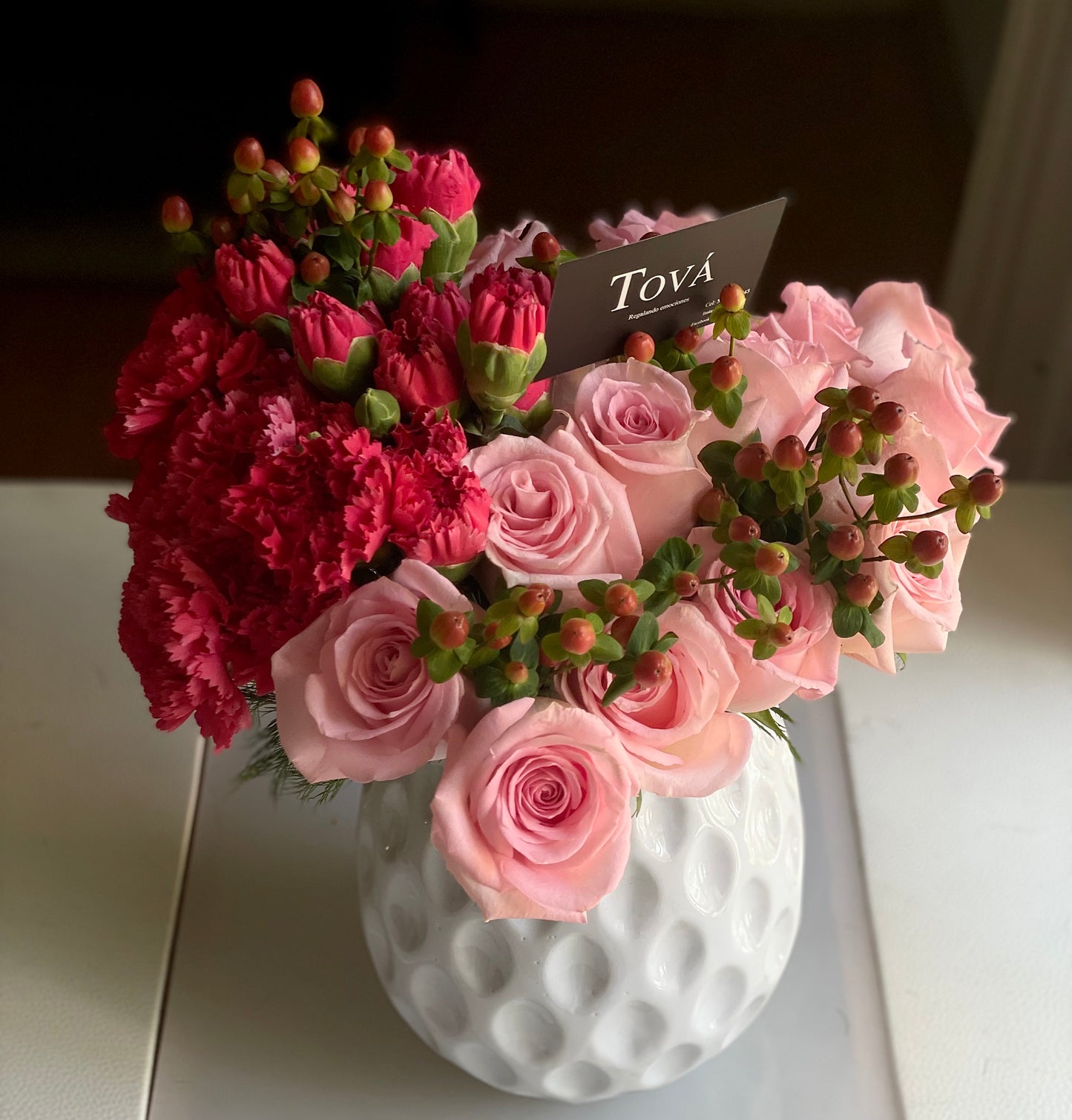 Arreglo de rosas con claveles y follaje, sobre florero de cerámica.