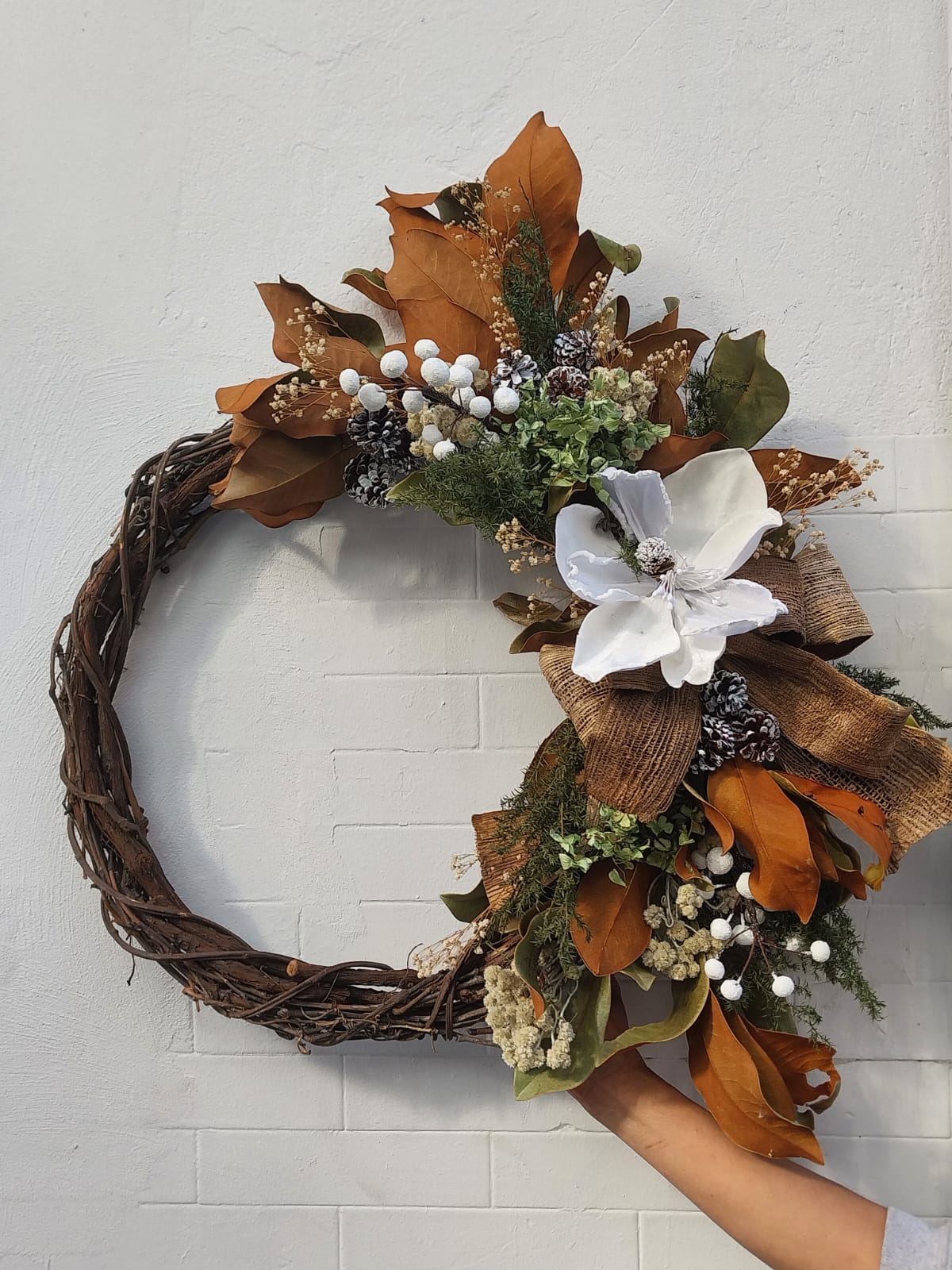 Corona navideña para pared o puerta hecha de flores y follaje preservado en base de madera.