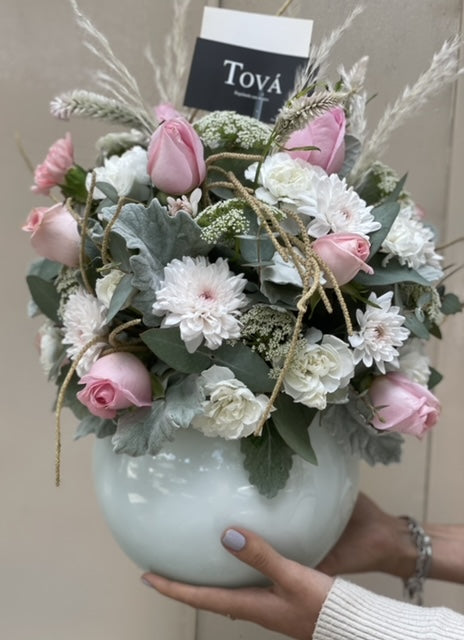 Arreglo de rosas con claveles y follaje, sobre florero de cerámica.