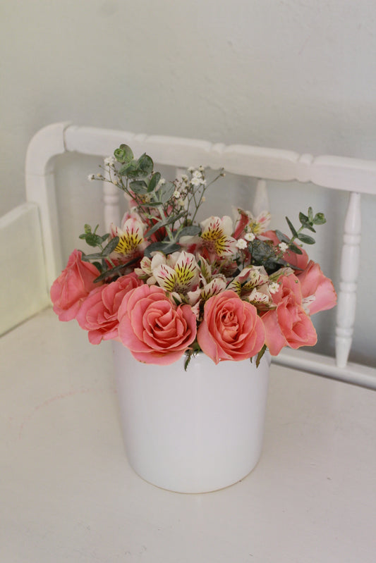 Rosas de invernadero con follaje sobre florero de cerámica.