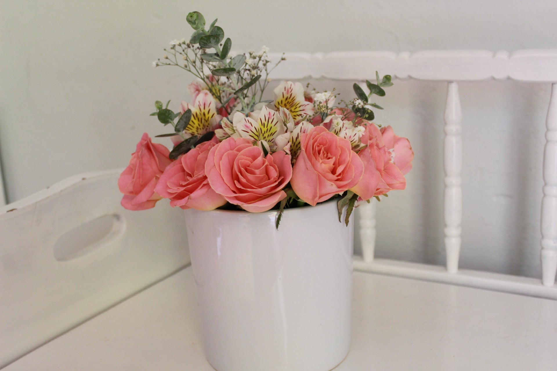 Rosas de invernadero con follaje sobre florero de cerámica.